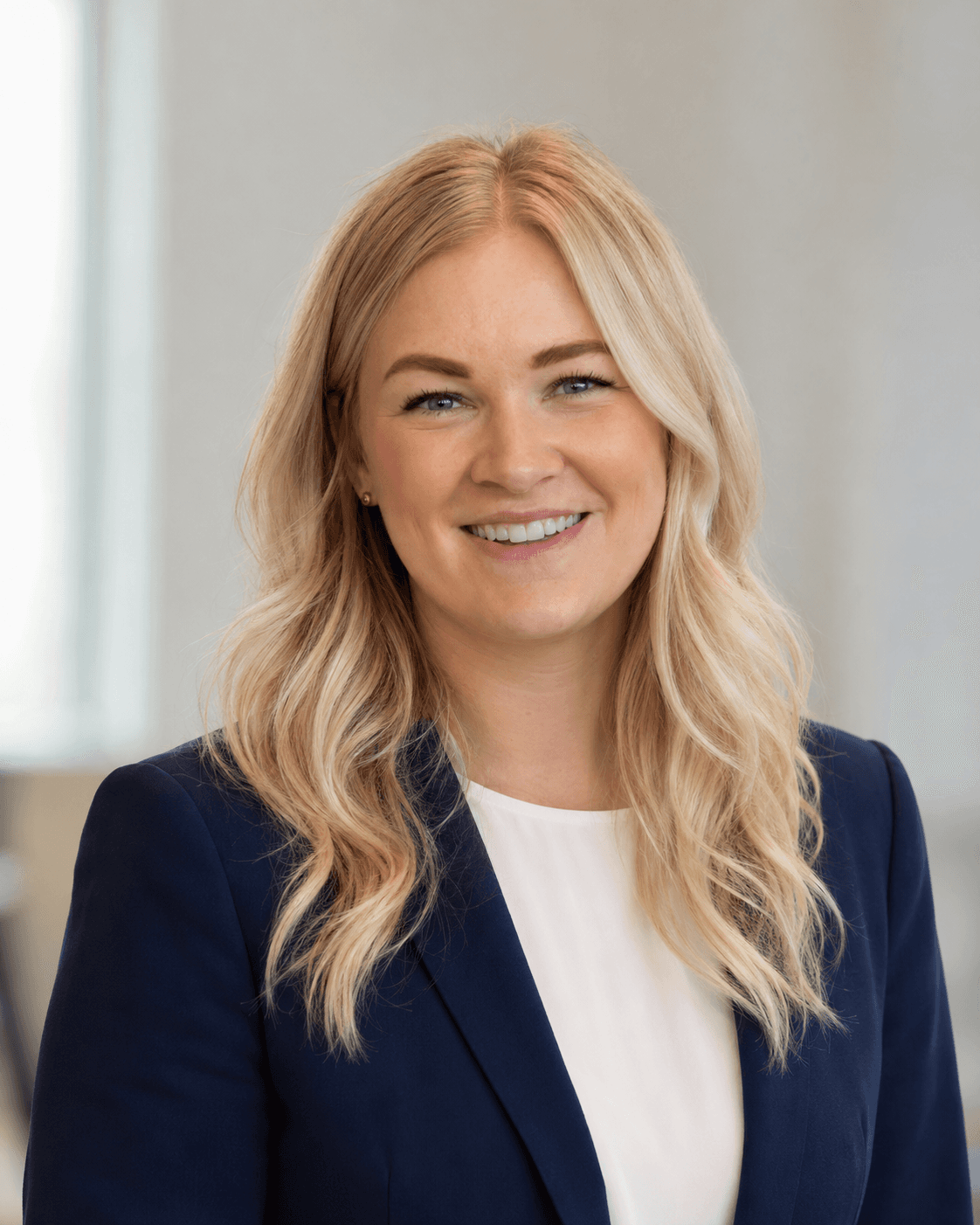 Smiling blonde woman with wavy hair wearing a navy blue blazer and white blouse.