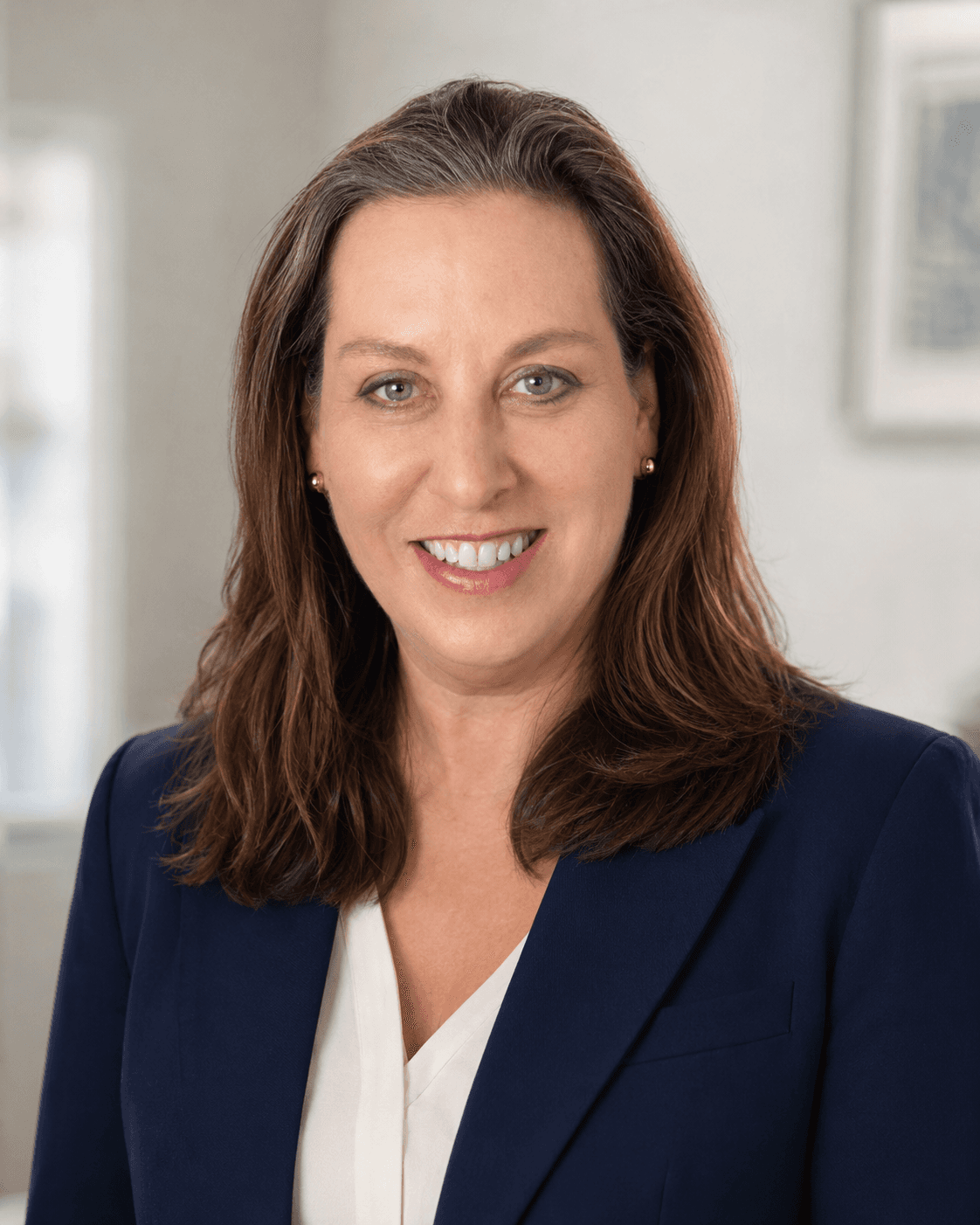 Professional headshot of a smiling woman with brown hair wearing a navy blue blazer.