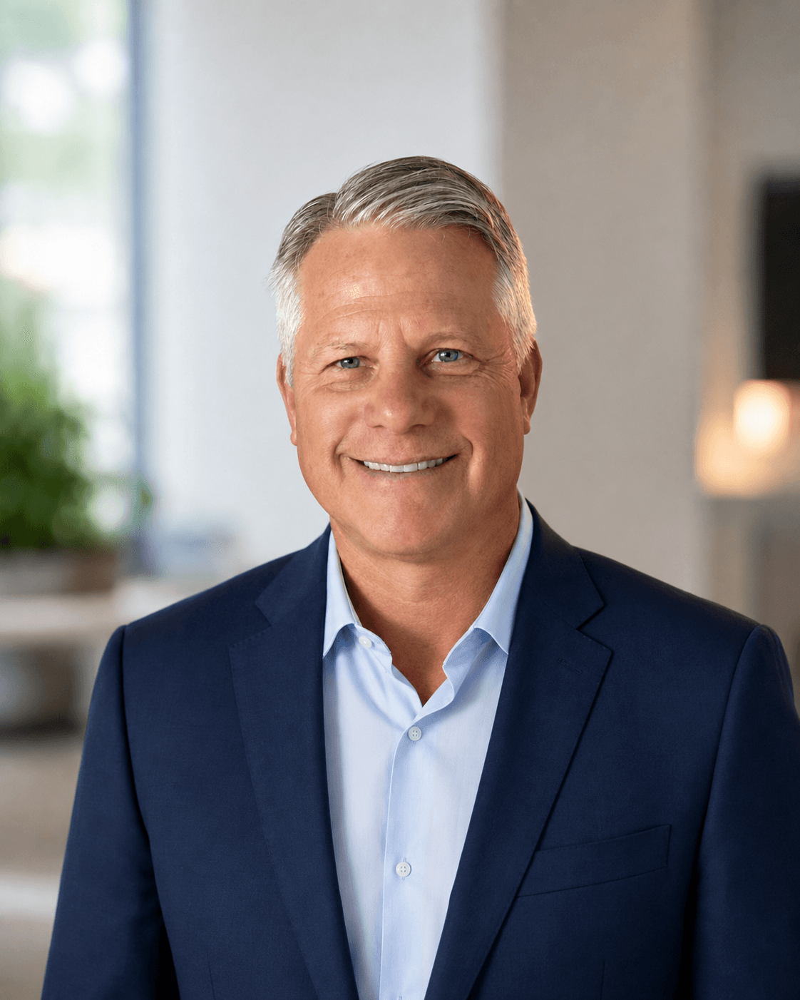 Smiling man with graying hair wearing a navy blue blazer and light blue dress shirt.